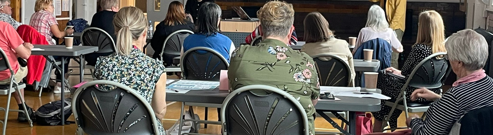 The backs of people sitting at tables watching a presentation