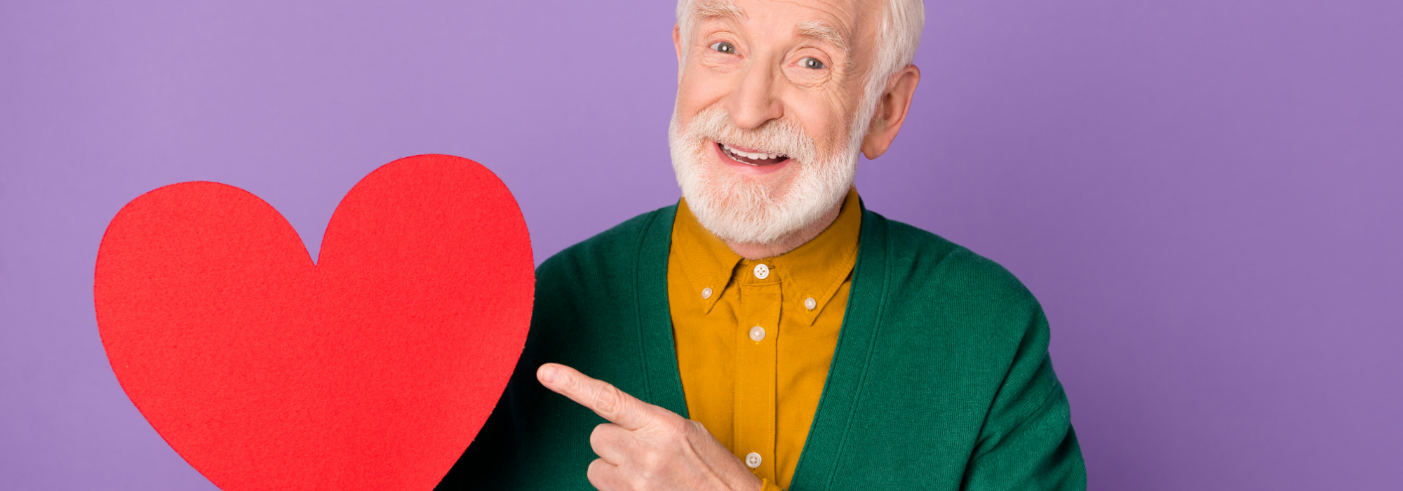 An older man smiling and pointing at a red paper heart