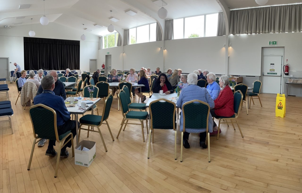 Photo of people sitting round tables talking in a community hall space